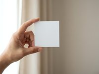 Hand holding blank white card against neutral beige background with soft natural light, suitable for business branding, marketing mockups, and promotional material design.
