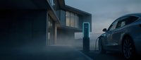 Modern electric vehicle charging at contemporary station during twilight hours with atmospheric mist and residential architecture in background.