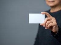 Man holding blank white business card in hand against gray background, suitable for corporate branding, marketing materials, and professional presentations.