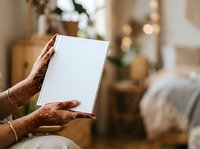 Hands holding blank white card in cozy bedroom with warm lighting and holiday decorations, suitable for greeting cards, invitations, and seasonal marketing campaigns.