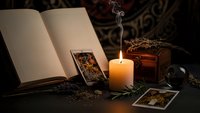Mystical tarot reading setup with burning candle, open book, cards and dried herbs creating atmospheric fortune telling scene for spiritual guidance.