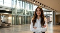 Professional businesswoman with crossed arms standing in modern corporate office lobby with glass windows and contemporary interior design.