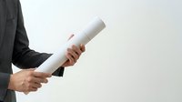 Professional holding rolled white document or diploma in hands, wearing dark business suit jacket against neutral background.