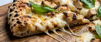 Freshly baked focaccia bread with charred spots, melted cheese, and fresh basil on wooden board, ready for serving or food photography.
