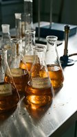 Laboratory flasks containing amber liquid with chemical formulas on labels, arranged on white surface for scientific research, education, and pharmaceutical development purposes.