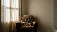 Cozy vintage leather armchair with knitted throw blanket in warm sunlit living room corner creating peaceful relaxing atmosphere for home decor.