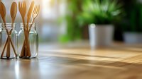 Wooden cutlery in glass jars on wooden table with natural light and blurred green plant background. Eco-friendly kitchen concept with sustainable utensils.