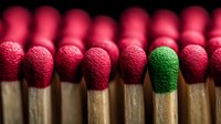 Green matchstick standing out among red ones, symbolizing individuality, uniqueness, and leadership concept against dark background.