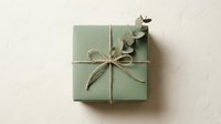 Sage green gift box tied with natural twine and eucalyptus leaves on neutral background for holidays and special occasions.
