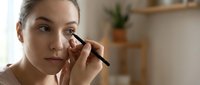 Young Caucasian woman applying eyeliner pencil, focused on eye makeup routine at home, beauty and self-care concept.