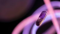 Transparent medical capsule pill with granules inside floating in purple neon lighting for pharmaceutical healthcare design concepts.
