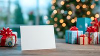 Blank greeting card on wooden table with wrapped Christmas presents and decorated tree with bokeh lights in background for holiday message.