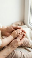 Elderly grandmother hands gently holding baby feet showing intergenerational love and family bonding in soft natural light by window.