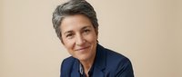 Confident mature businesswoman with short gray hair smiling warmly in professional navy blazer against neutral background for corporate communications.