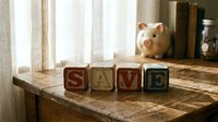 Wooden alphabet blocks spelling SAVE on rustic table with piggy bank in background, representing financial planning and money saving concepts.