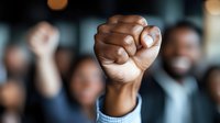 Raised fist of African American person at protest rally or demonstration, symbol of solidarity, resistance and unity against social injustice, crowd background.