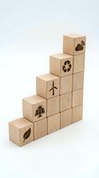 Wooden blocks stacked in ascending staircase pattern with renewable energy and sustainability icons including wind turbine, solar panel, recycling symbol, leaf, and wifi signal for eco-friendly concepts.