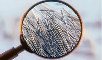 Extreme macro photography through magnifying glass shows metallic needles or pins creating abstract geometric pattern with selective focus and blur.