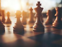 Wooden chess pieces on board in warm sunlight with dramatic shadows, king and pawn figures in focus against blurred background create strategic composition.