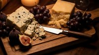 Assorted gourmet cheeses with fresh figs and dark grapes arranged on wooden board, ideal for food styling, culinary content, and entertaining concepts.