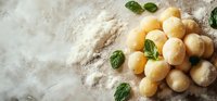 Raw homemade potato gnocchi dumplings with fresh basil leaves and flour on rustic wooden surface, traditional Italian cuisine preparation.