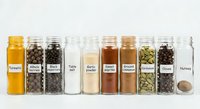 Organized spice collection in glass jars with labels including turmeric, black pepper, salt, garlic powder, paprika, cinnamon and nutmeg on white background.