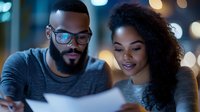 Young African American couple reviewing documents together at night, illuminated by soft bokeh lights, expressing positive emotions while analyzing papers.
