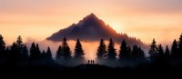 Panoramic mountain silhouette at sunset with fog rolling through pine forest and three hikers standing on hill watching dramatic orange sky.