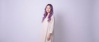 Young Asian woman in white dress standing against purple gradient background with peaceful expression and long wavy hair for lifestyle photography.
