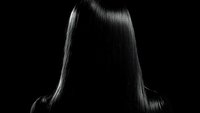 Silky smooth straight hair illuminated against dark background, creating dramatic contrast with light highlighting the shine and texture of healthy locks.