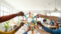 Young diverse professionals joining hands around colorful molecular structure model in bright office space, symbolizing teamwork, innovation, collaboration, and scientific research partnership.
