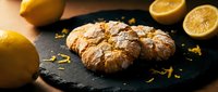Freshly baked lemon crinkle cookies on dark slate with citrus zest and orange slices. Homemade dessert perfect for bakery menus and food blogs.