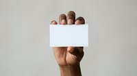 Group of diverse hands holding blank white card for message or promotion on neutral background.