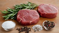 Raw beef tenderloin steaks with fresh rosemary sprigs, sea salt crystals and mixed peppercorns on wooden cutting board, food preparation concept.