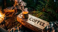 Steaming metal mug on a rustic wooden sign reading Coffee beside a campfire in a forest, evoking outdoor adventure and cozy wilderness mornings.