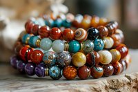 Colorful gemstone beaded bracelets with natural stones including turquoise, carnelian, amethyst and jasper arranged on rustic wooden surface for jewelry making.