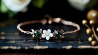 Elegant rose gold bracelet with white flower charm and green gemstone accents on dark surface with soft bokeh lights creating luxurious jewelry display atmosphere.