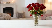 Red roses bouquet in crystal vase on white table in cozy living room with fireplace and warm lighting for romantic home decor and special occasions.