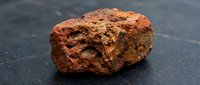Red porous volcanic rock specimen with rough textured surface on dark slate background for geology education and natural science studies.