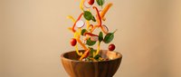 Fresh vegetables falling into wooden bowl with dynamic motion splash effect for healthy cooking and nutrition concepts.
