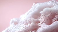 Luxurious white foam bubbles on pink background, macro photography showing delicate soap suds texture with soft lighting creating dreamy atmosphere.