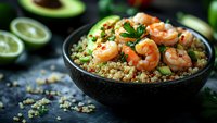Grilled shrimp with quinoa, avocado, and lime in black ceramic bowl on dark background. Fresh herbs and citrus garnish create appetizing healthy meal.