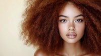Young African American woman with natural curly afro hair and glowing skin against beige background, fashion and beauty portrait with soft lighting.