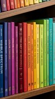 Colorful books arranged on wooden shelves creating rainbow spectrum from purple to blue. Library organization system for education and learning environments.