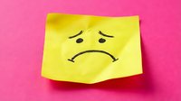 Yellow sticky note with sad face drawing on bright pink background expressing negative emotions and mental health awareness for office communication.
