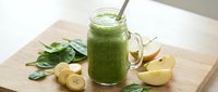 Fresh green smoothie in mason jar with spinach leaves, sliced banana and apple on wooden cutting board. Healthy breakfast drink for detox and wellness lifestyle.