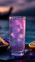 Sparkling purple cocktail with bubbles in tall glass garnished with edible flowers and citrus, glowing in evening light against dark moody background.