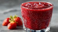 Fresh strawberry smoothie in glass with whole berries on dark surface for healthy breakfast drinks and summer refreshment recipes.