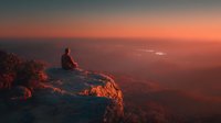 Person sitting on mountain cliff edge watching dramatic sunset over valley landscape with warm orange and pink sky colors creating peaceful meditation moment.
