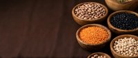 Assorted legumes and beans in wooden bowls on dark surface for healthy cooking and nutrition concepts.